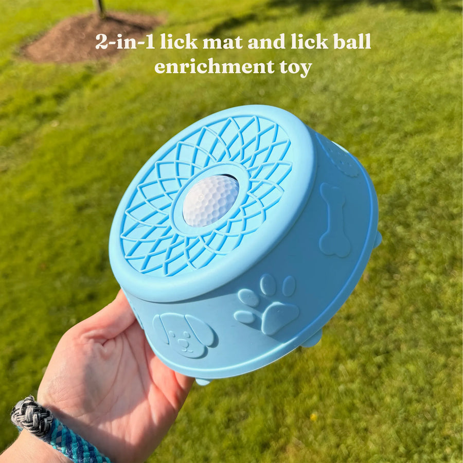 Hand holding the blue Hush Bowl dog lick bowl outdoors, showing its lattice lick mat lid and rolling centre ball